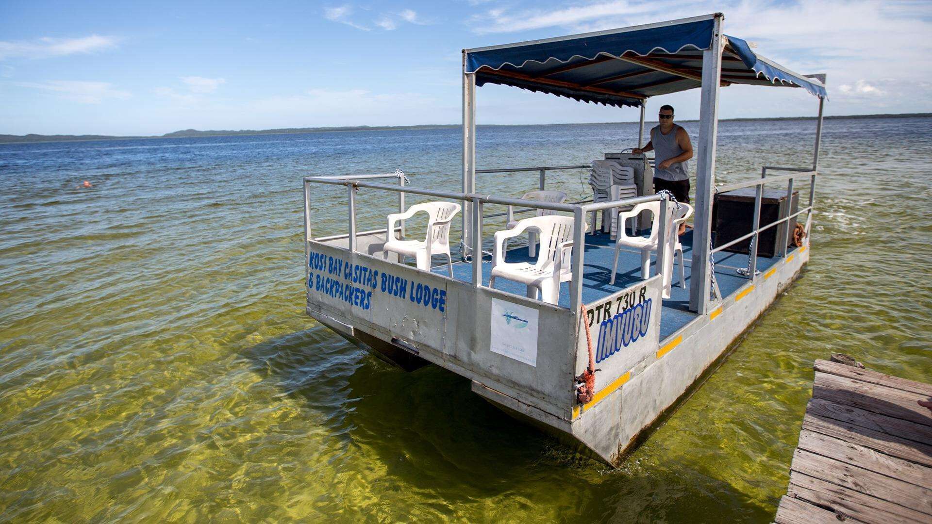 Um barco com área de estar coberta e placa indicando ser uma pousada rústica para mochileiros.