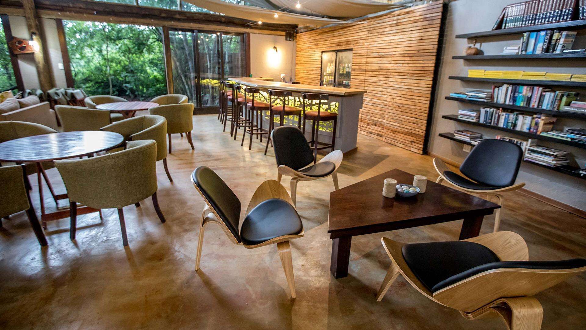 A cozy indoor space with round tables and chairs, a bar area, and a bookshelf filled with books.