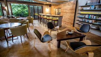 A cozy indoor space with round tables and chairs, a bar area, and a bookshelf filled with books.