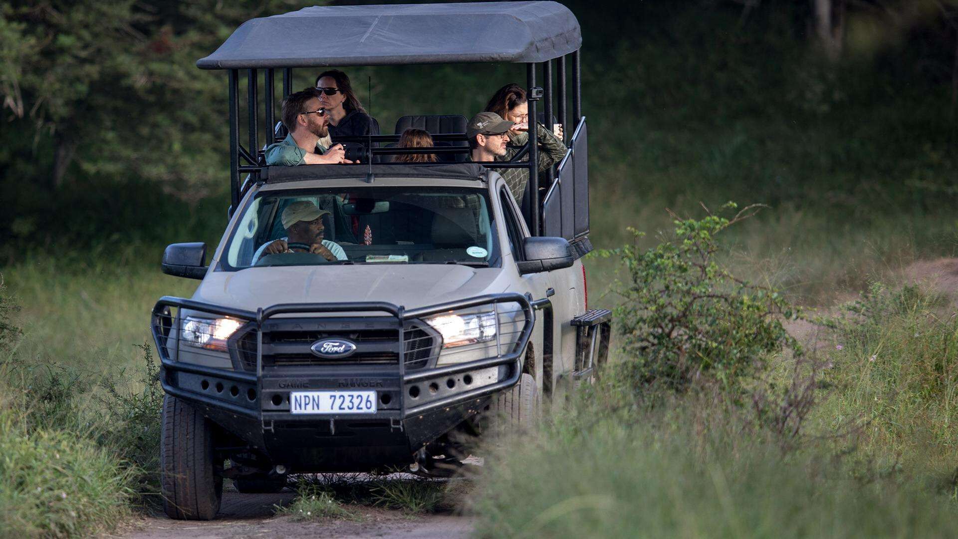 A rugged off-road vehicle with a roof rack, driving on a dirt path surrounded by greenery.