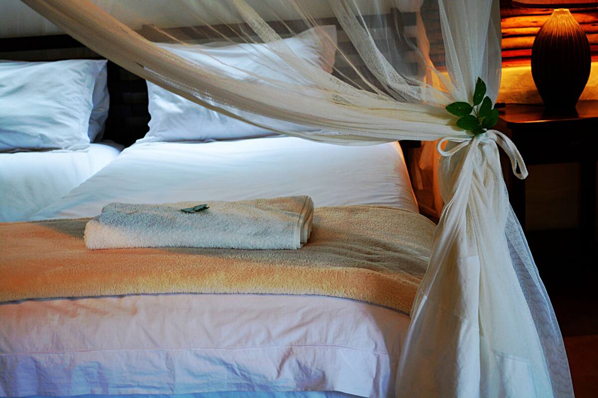 A neatly made bed with a folded towel, white bedding, and a canopy.