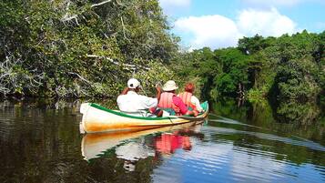 Een boot met twee passagiers op een kalme rivier, omringd door weelderige begroeiing.