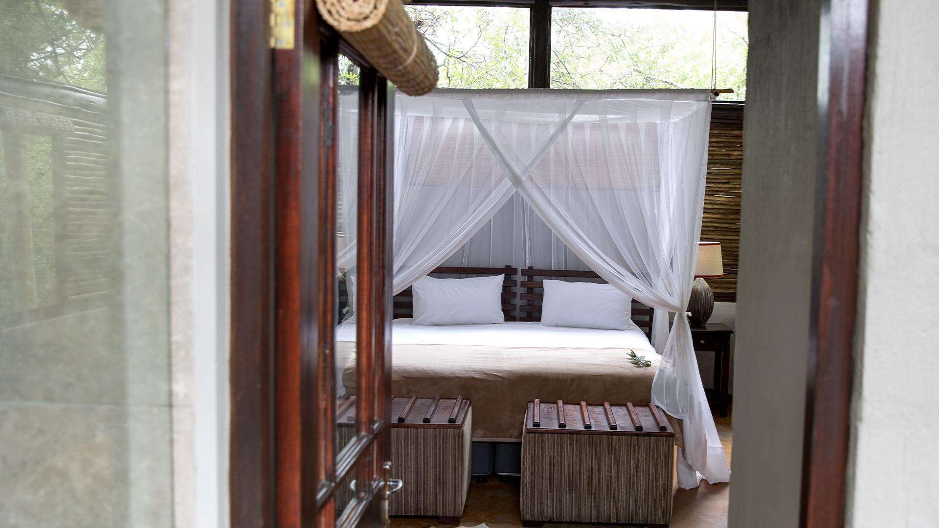 A bedroom with a bed, white curtains, and a wooden headboard.