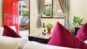 A room with a red door, a window with curtains, a table with wine glasses and a bottle, and a potted plant. - The Cockatoo Nature Resort & Spa (Siem Reap)