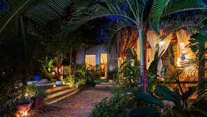 A well-lit garden area with a pathway leading to a building, surrounded by various plants and trees. - The Cockatoo Nature Resort & Spa (Siem Reap)
