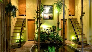 A tranquil indoor garden with a central pond, surrounded by bamboo plants and a wooden staircase. - The Cockatoo Nature Resort & Spa (Siem Reap)