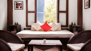 A room with a bed, two nightstands, wicker chairs, a table with a glass, and a window with blue shutters. - The Cockatoo Nature Resort & Spa (Siem Reap)