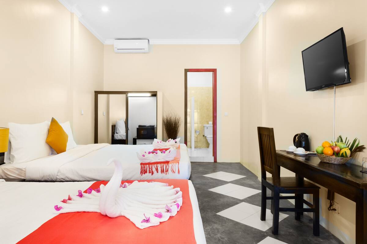 Quarto de hotel com uma cama, uma mesa com uma cesta de frutas, uma televisão e um espelho.