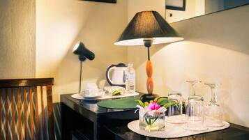 A hotel room with a desk, a lamp, a mirror, a vase with flowers, and a tray with glasses and a water bottle.