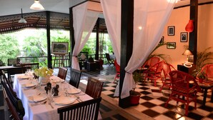 A dining area with a checkered floor, tables set with white tablecloths, and red chairs. - The Cockatoo Nature Resort & Spa (Siem Reap)