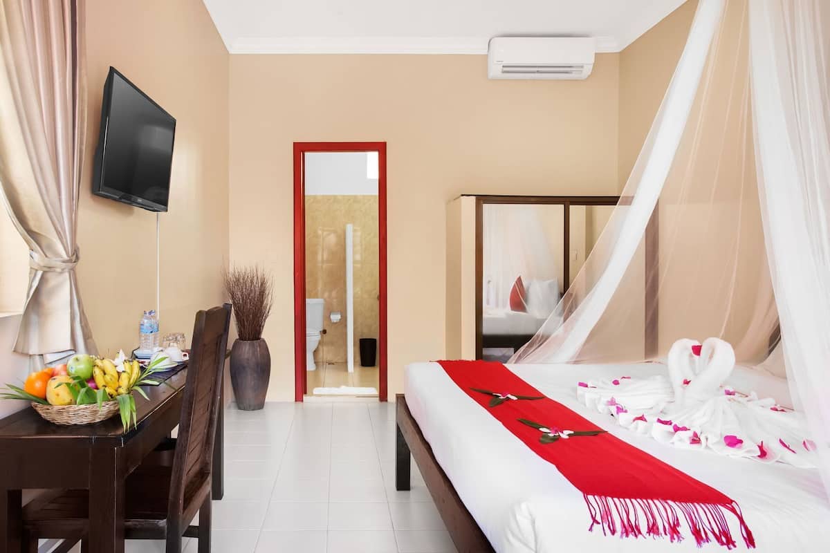 Quarto de hotel com cama, secretária com cesta de frutas, televisão e banheiro visível por uma porta.
