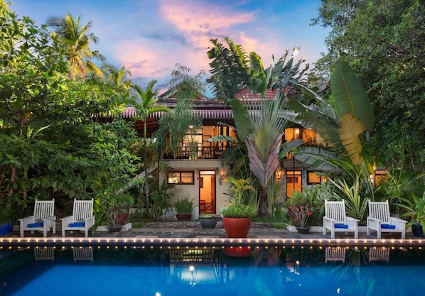 A poolside area with lounge chairs, a pool, and a building with a traditional architectural style. - The Cockatoo Nature Resort & Spa (Siem Reap)