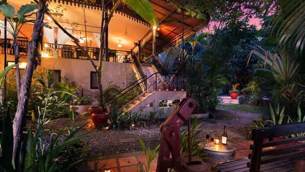 A well-lit outdoor area with a wooden bench, a table with candles, and a staircase leading to an upper level. - The Cockatoo Nature Resort & Spa (Siem Reap)