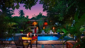 A pool area with lounge chairs and a table, surrounded by tropical plants and a building in the background. - The Cockatoo Nature Resort & Spa (Siem Reap)