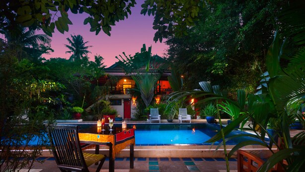A pool area with lounge chairs and a table, surrounded by tropical plants and a building in the background. - The Cockatoo Nature Resort & Spa (Siem Reap)