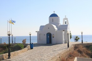 A white church with a blue dome and a bell tower, located near the sea with a clear sky.
