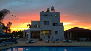 Un edificio moderno con zona de piscina, incluyendo sillones de descanso y sombrillas.