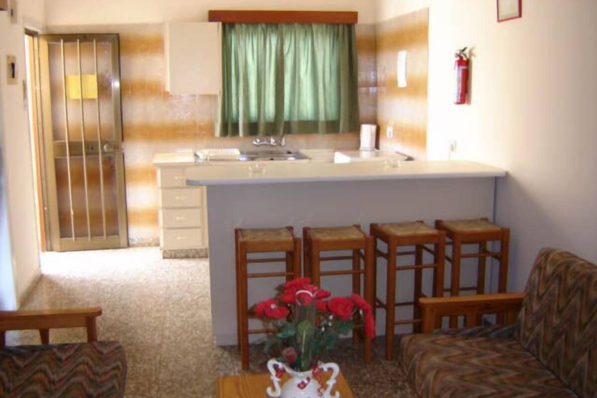 A compact living space with a kitchenette, a dining area with four wooden stools, and a sofa.
