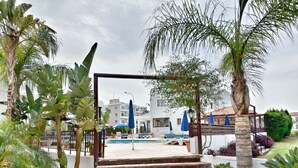 Un área de piscina con escalones que conducen a un espacio de descanso cubierto, rodeado de palmeras y plantas en macetas.