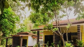 A two-story building with a yellow and brown facade, surrounded by lush greenery and trees.