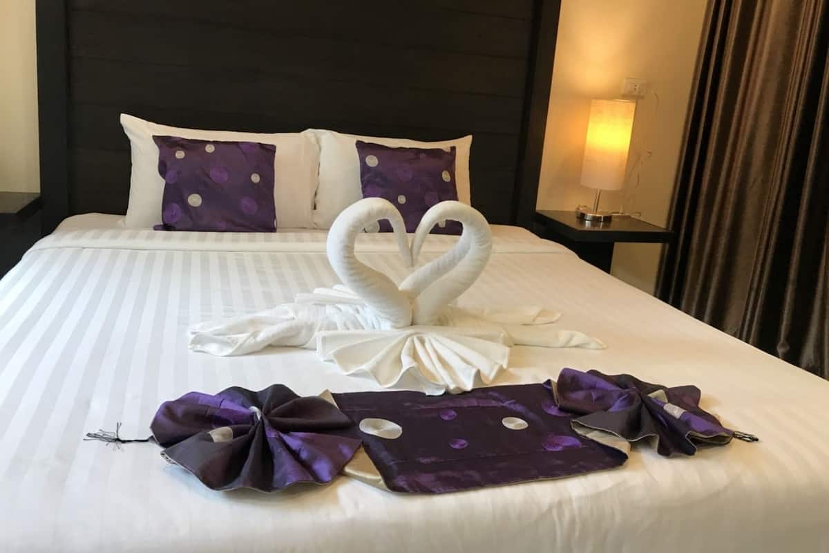 A hotel room with a neatly made bed, two pillows, a nightstand with a lamp, and a window with curtains.