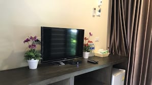 Un televisor de pantalla plana sobre un mueble de madera con plantas en macetas, un control remoto y un refrigerador pequeño.