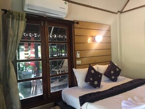 A hotel room with a bed, pillows, a bedside table, a window with curtains, an air conditioning unit, and a wall-mounted light fixture. - Lipe Sunset Forest Resort (Koh Lipe)