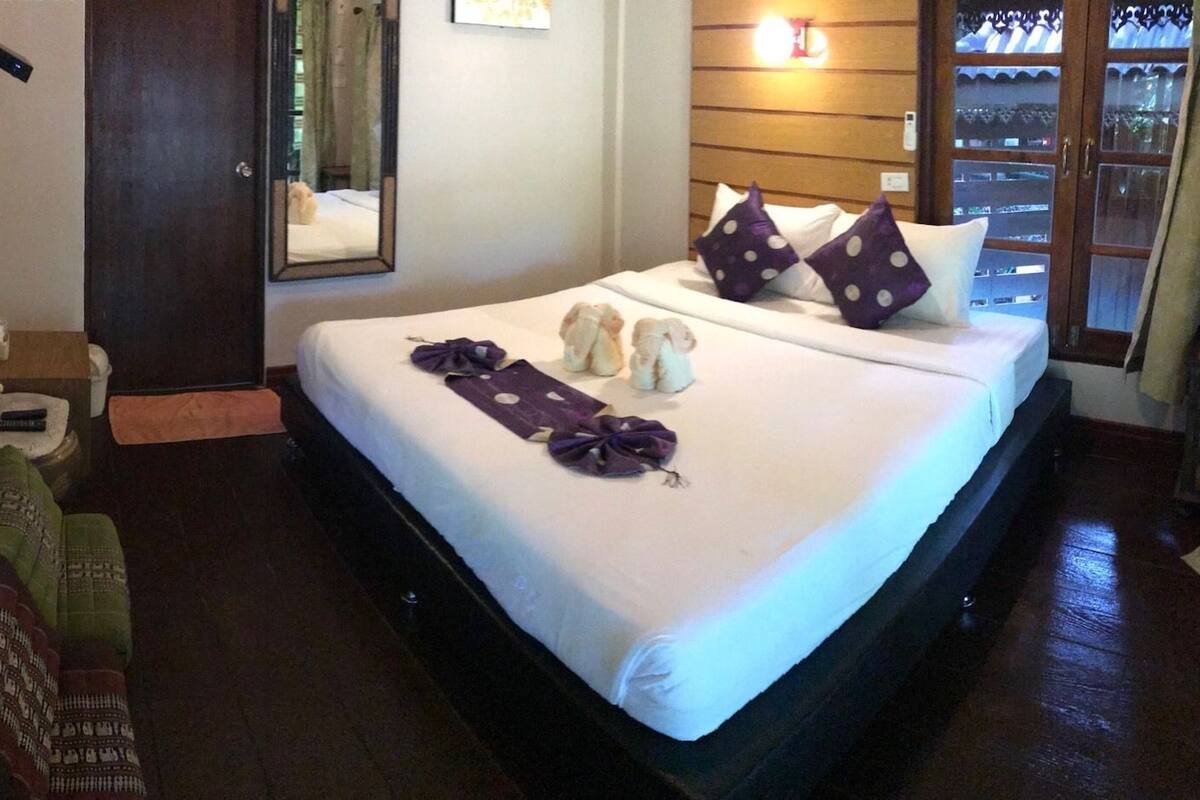 A hotel room with a bed, pillows, a bedside table, a mirror, and a wall-mounted TV.