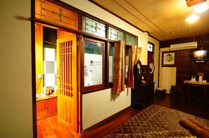 Ein traditionell eingerichtetes Zimmer mit Holzboden, einem gemusterten Teppich, einem Bett, einem Schreibtisch mit Lampe und einem Fernseher.