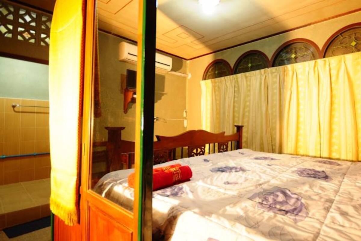 Un dormitorio con una cama de madera, una ventana con cortinas y un aire acondicionado instalado en la pared.