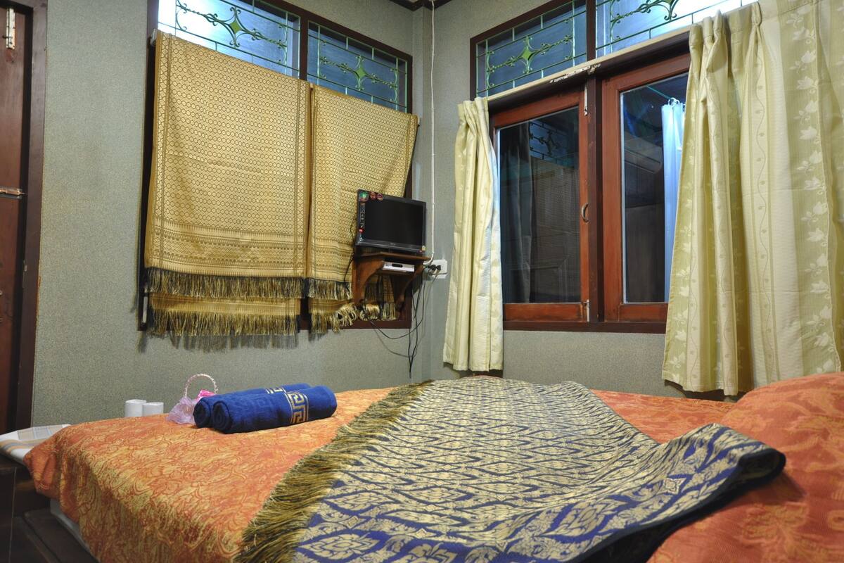 Una habitación con una cama, un televisor sobre un mueble bajo y un ventanal con cortinas.