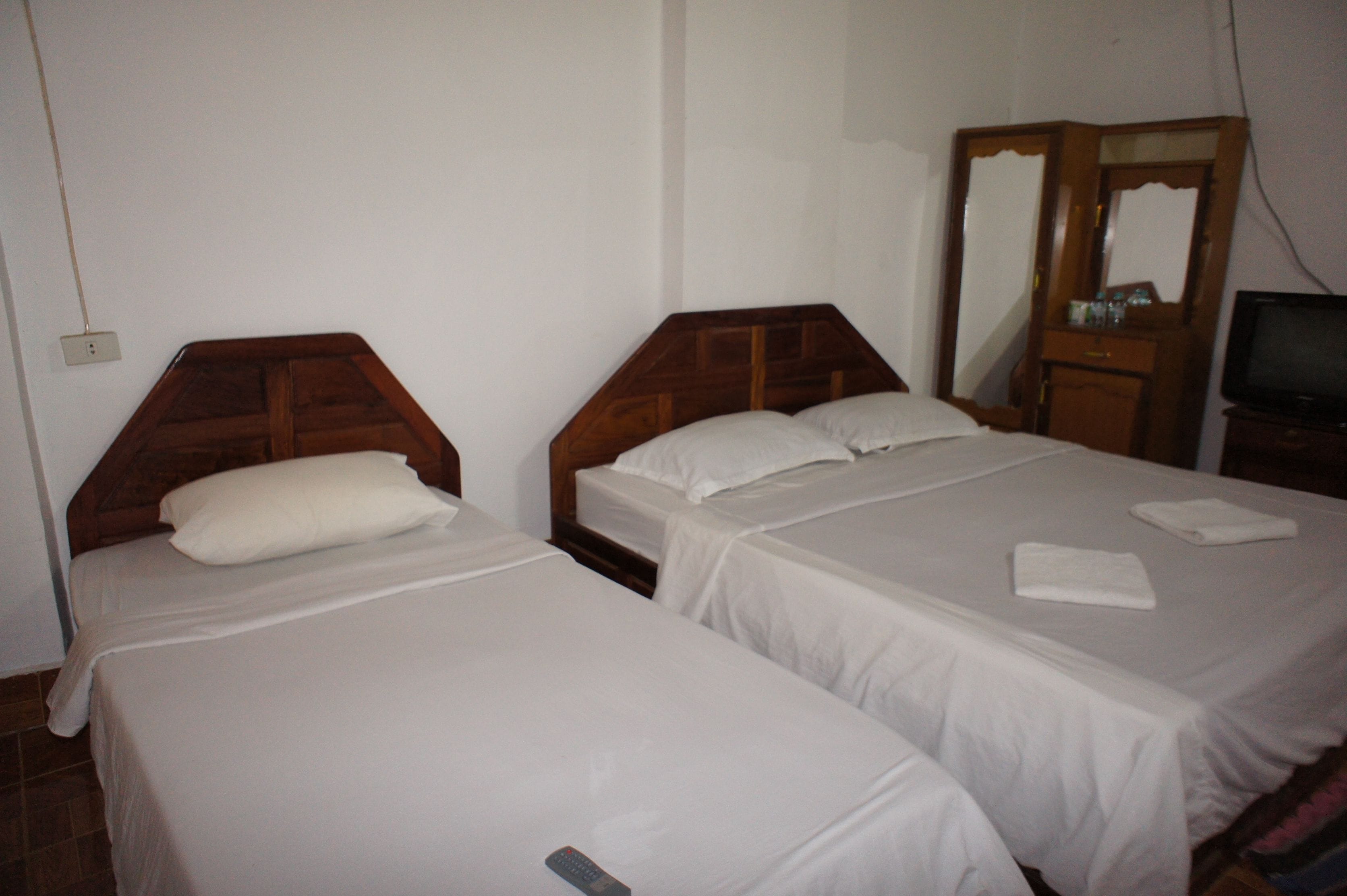 A hotel room with two single beds, a wooden headboard, a mirror, a television, and a small dresser.