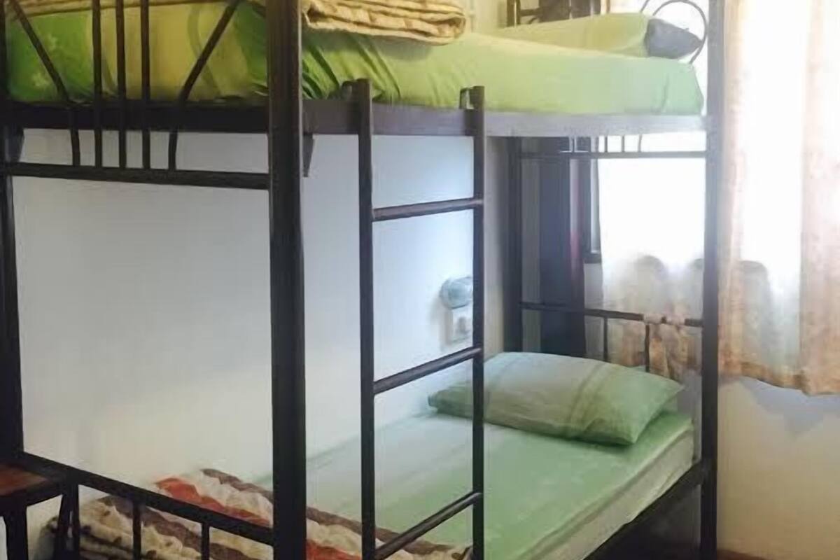 Dormitorio con literas, suelo de madera y ventana con cortinas.