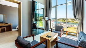 Hotelkamer met een groot raam, een flatscreen televisie, een houten bureau en twee grijze gestoffeerde fauteuils.