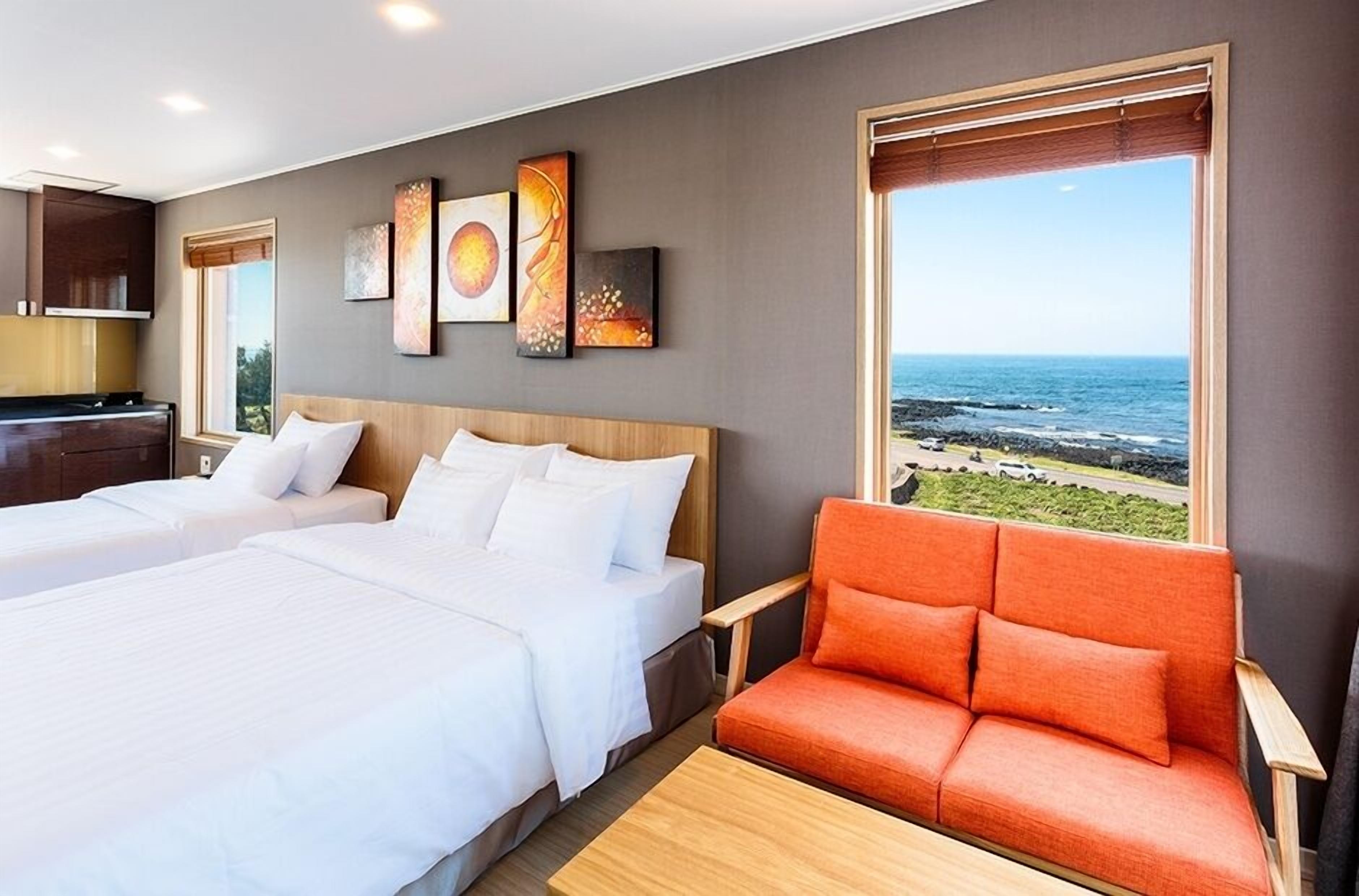 Une chambre d’hôtel avec deux lits, un canapé et une grande fenêtre donnant sur l’océan.