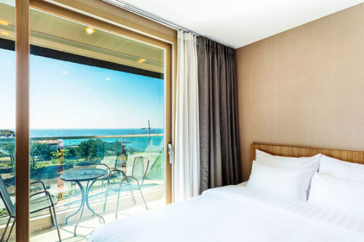Een hotelkamer met een ruim balkon, een bed met witte lakens en uitzicht op de oceaan.