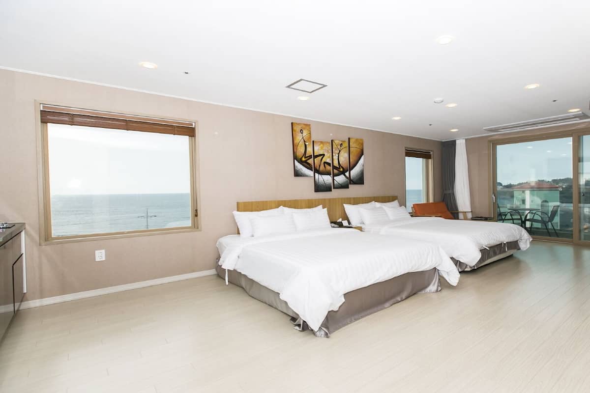 Een ruime slaapkamer met twee bedden, grote ramen, een balkon en uitzicht op zee.