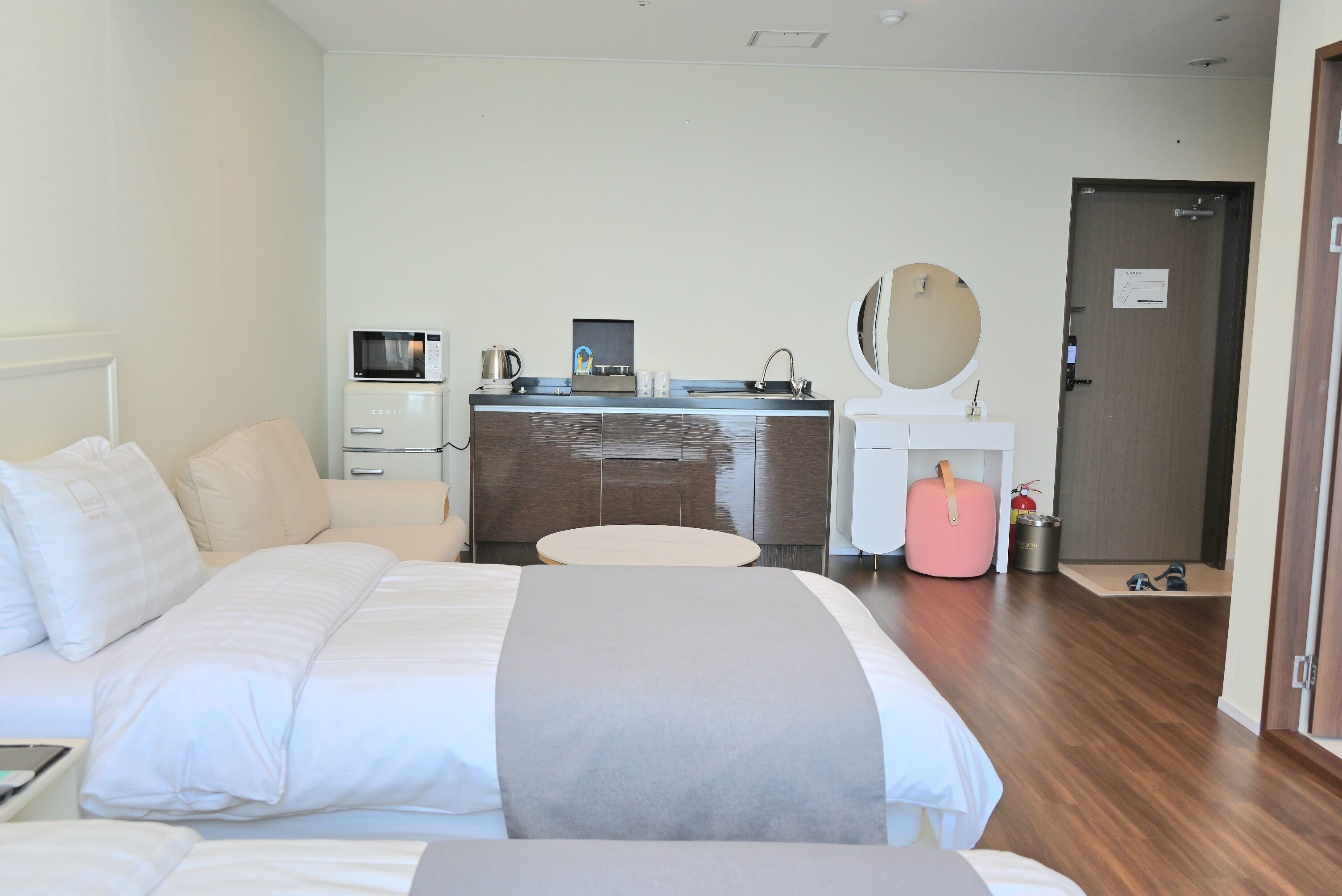 Ein Hotelzimmer mit Bett, Nachttisch, Schreibtisch mit Computer, Mikrowelle, Spüle und Spiegel.