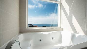 Un baño moderno con una bañera grande, una ventana con vistas al mar y una zona de ducha.