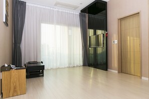 Una habitación moderna con un escritorio de madera, una mesa negra y un gran ventanal con cortinas translúcidas.