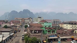 Vista de la calle con edificios, una carretera y montañas al fondo.