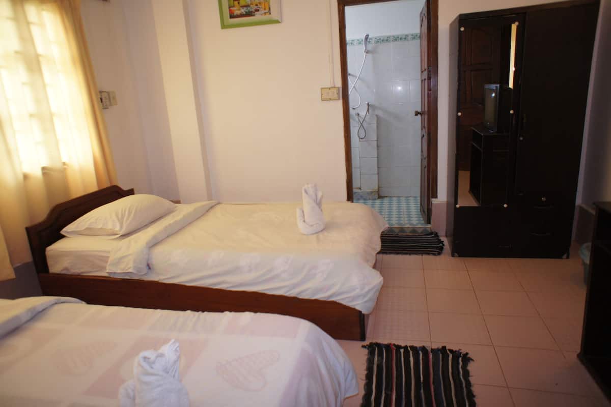 A hotel room with two beds, a shower area, and a television.