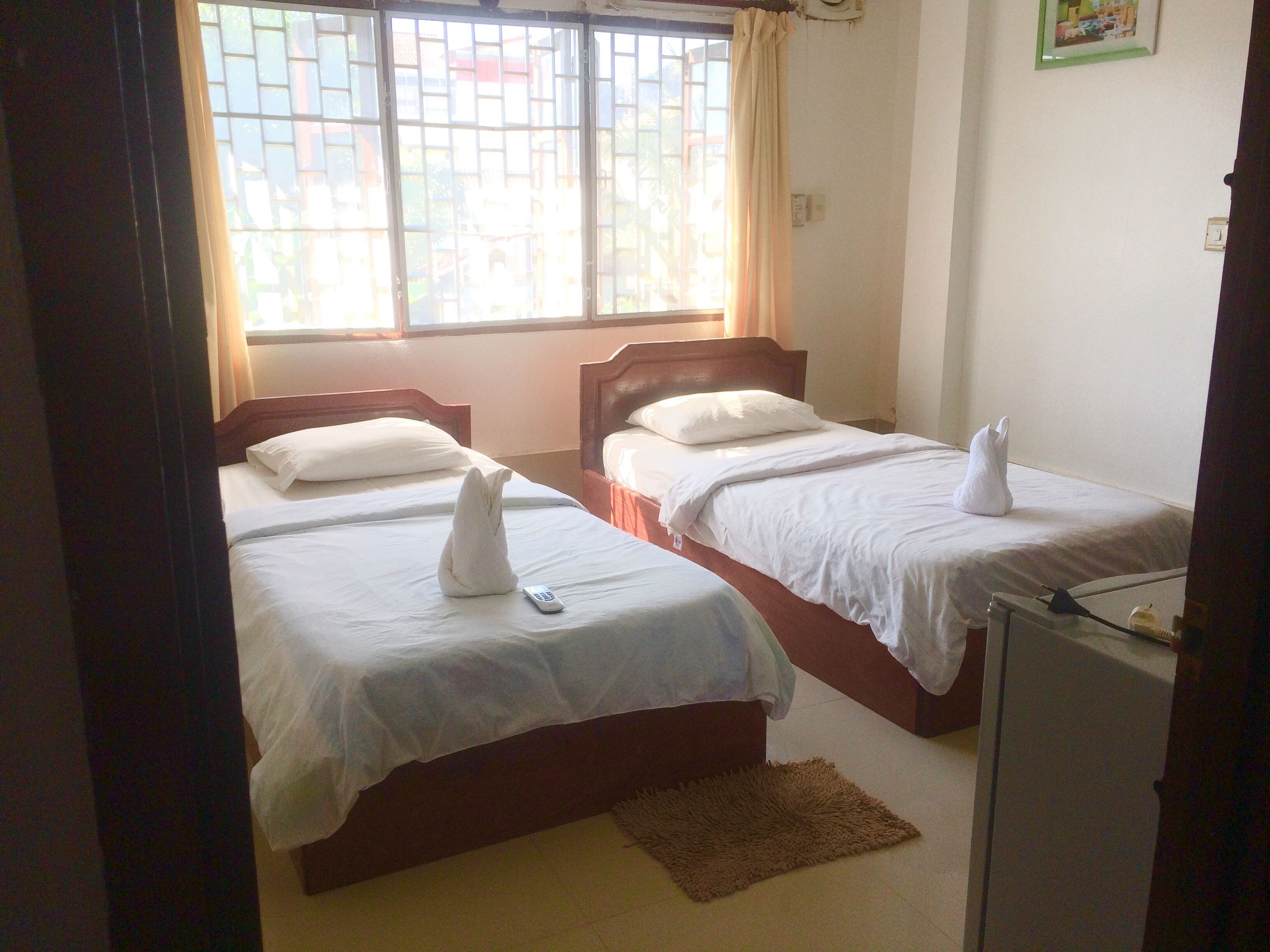 A hotel room with two beds, a window with curtains, a small rug, and a television.
