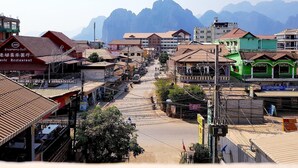 Vista de una calle en un pueblo con edificios, un restaurante y montañas al fondo.