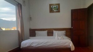Un dormitorio con cama, cabecera de madera, ventana con cortinas, puerta y un cuadro en la pared.