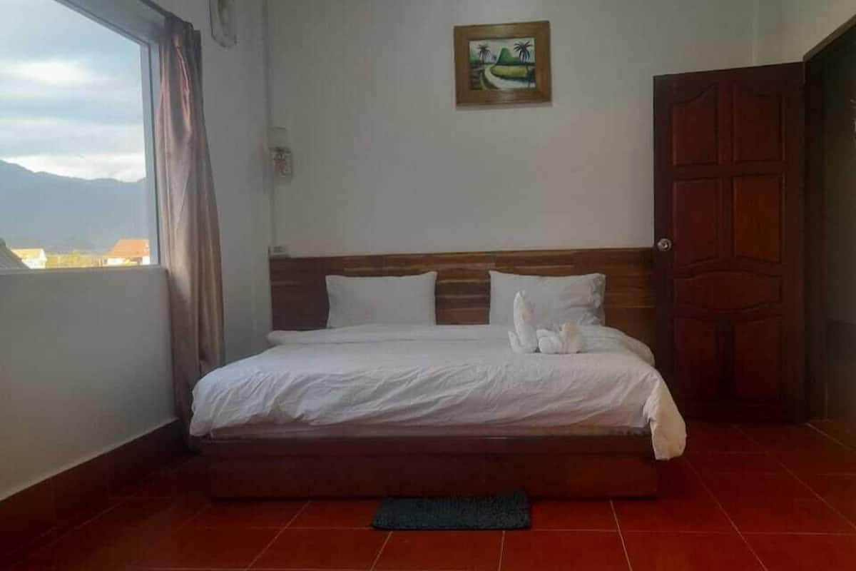 A bedroom with a bed, a wooden headboard, a window with curtains, a door, and a painting on the wall.