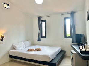 A hotel room with a bed, a desk with a television, and two windows with curtains. - Harmony Bed and Bakery (Koh Lipe)