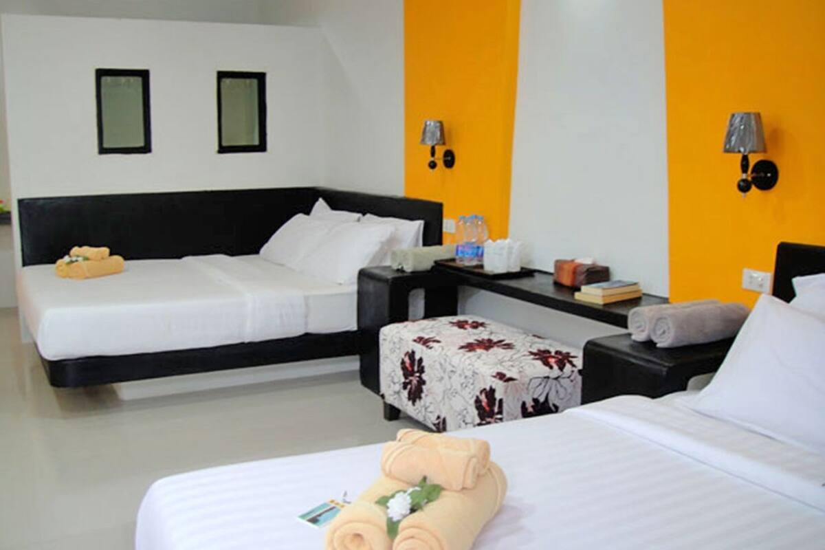 A hotel room with two beds, a desk, and a chair. There are towels on the beds and a small table with a lamp.