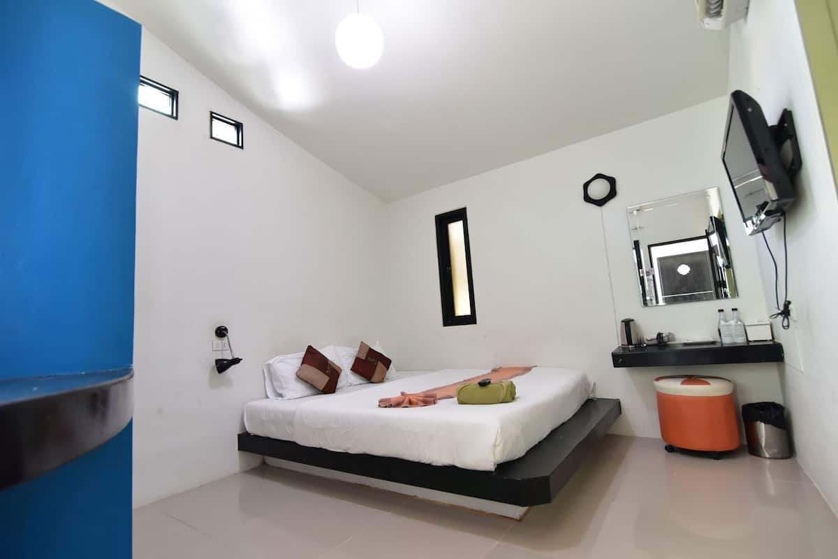 A bedroom with a bed, a small window, a mirror, a sink, and a trash bin.