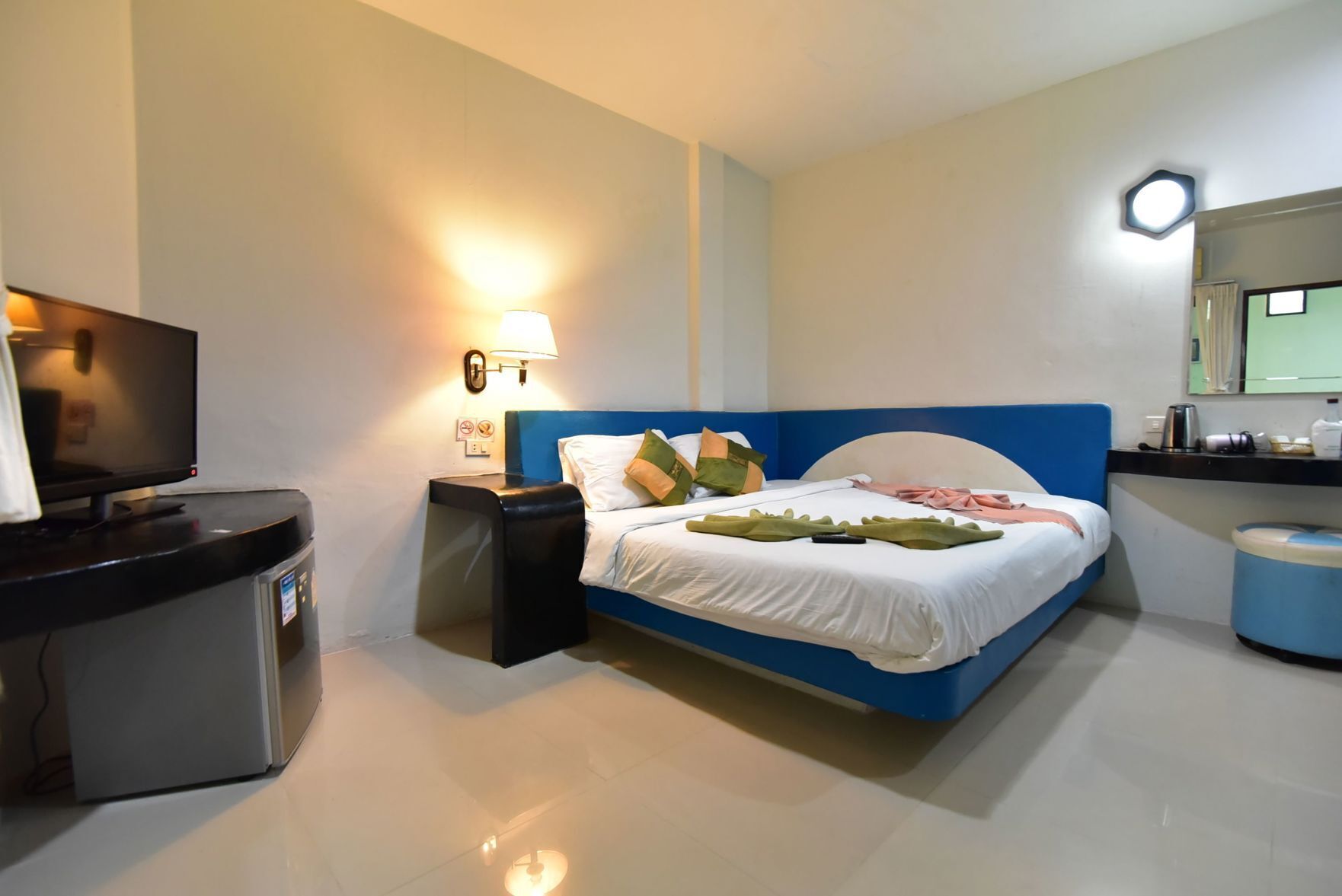 Ein Hotelzimmer mit Bett, Schreibtisch mit Fernseher, Nachttisch, Lampe und Spiegel.
